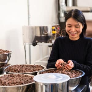 A smiling woman holds a handful of cacao beans